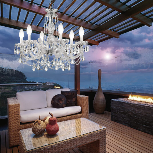 A rooftop patio showcases wicker furniture and a glass table by a crackling fireplace. The Crystal Glass Outdoor Chandelier elegantly hangs from a wooden pergola, casting shimmering reflections as the vibrant sunset and stunning city views provide a breathtaking backdrop.