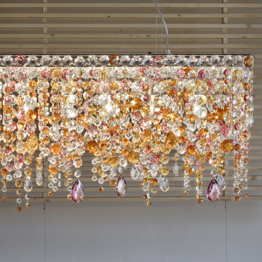 Contemporary Rectangular Multicoloured Crystal Chandelier The Contemporary Rectangular Multicoloured Crystal Chandelier, adorned with vibrant crystal beads in shades of orange, pink, and clear, hangs elegantly from the ceiling, casting a shimmering display against a wooden slat background.