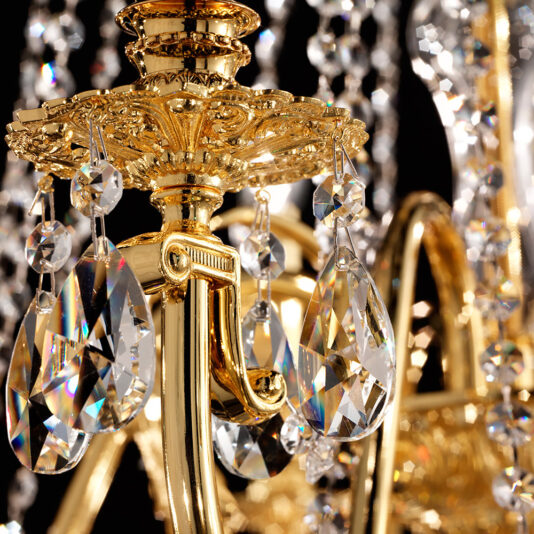 Close-up of a luxurious Large Italian Gold Plated Crystal Chandelier with intricate detailing and shimmering teardrop Swarovski crystal pendants that capture light, enhancing its opulence against a dark backdrop.