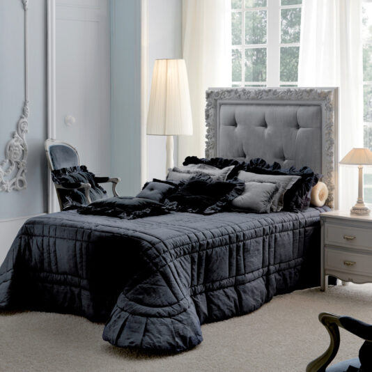 A stylish bedroom features a plush gray bedspread on the Classic Reproduction Button Upholstered Bed adorned with decorative pillows. Against a light-colored wall with intricate detailing, a standing lamp and nightstand with a small lamp add a soft glow, enhancing the serene ambiance.
