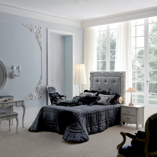 A stylish bedroom featuring the Classic Reproduction Button Upholstered Bed with gray bedding. The room exudes a vintage aesthetic with ornate wall decorations, a cushioned armchair, and matching bedside table and vanity. Large windows allow natural light to fill the space, complemented by a floor lamp that adds to the ambiance.