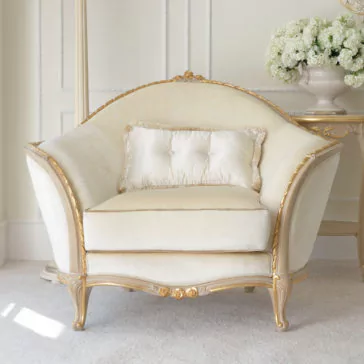 Cream And Gold Reproduction Louis Armchair A luxurious Cream And Gold Reproduction Louis Armchair with ornate detailing stands in an elegantly decorated room. A matching pillow rests on the chair. Behind it, a side table with a large vase of white flowers completes the sophisticated setting.