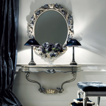French Rose Wall Fixing Console Table An ornate vanity setup featuring an oval mirror in an intricate frame, accompanied by two black-shaded lamps and the French Rose Wall Fixing Console Table. On the console table is a vase filled with dark flowers, and a stool with a cushioned seat is partially visible on the right.