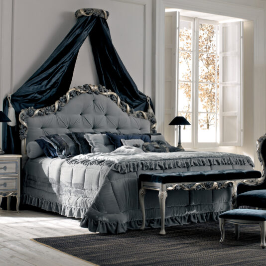 Luxurious bedroom featuring the High End Italian Rose and Ribbon Button Upholstered Bed with a dark blue velvet canopy, matching bedding, and vintage furniture. Sunlight pours through a large window, enhancing the room’s timeless elegance.