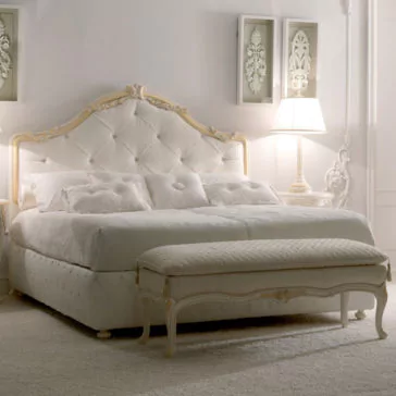 Italian Rose Detail Luxury Bed A luxurious bedroom featuring the Italian Rose Detail Luxury Bed, a plush, tufted white bed with an ornate rose detail headboard and a matching bench at the foot. Textured white pillows and a quilted comforter adorn the bed. Elegant white decor, including a lamp and framed artwork, complete the serene, sophisticated look.