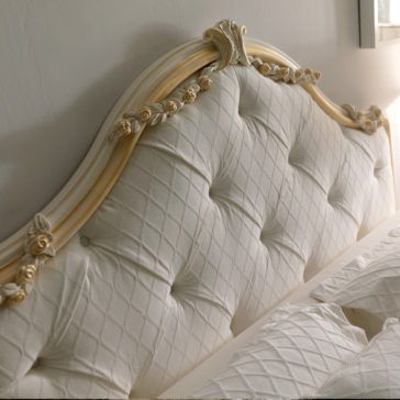 Italian Rose Detail Luxury Bed Here is a close-up view of the Italian Rose Detail Luxury Bed, featuring an elegant cream-colored tufted headboard adorned with intricate Italian rose details and a quilted fabric design. The luxury bed is partially covered with a white, textured bedspread as sunlight streams in from a nearby window.