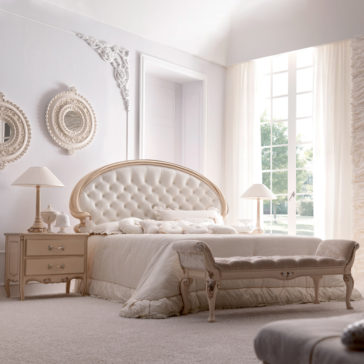 Opulent Italian Swirl Gold Button Upholstered Bed A luxurious, elegant bedroom features the Opulent Italian Swirl Gold Button Upholstered Bed, dressed in cream-colored bedding, and complemented by a matching bench at the foot. The room is adorned with ornate mirrors, stylish nightstands with lamps, and a large window with sheer curtains allowing ample natural light.