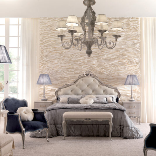 Reproduction Italian Bedroom Bench Luxurious bedroom with a tufted headboard bed, flanked by two ornate nightstands and modern table lamps. A Reproduction Italian Bedroom Bench sits at the foot of the bed. The textured wall and elegant chandelier add sophistication, and a large window fills the room with natural light.