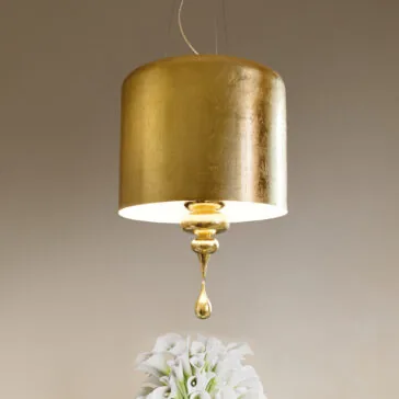 A Modern Italian Designer Gold Leaf Ceiling Light with a cylindrical shade and ornate drop detail illuminates white calla lilies against a warm background.