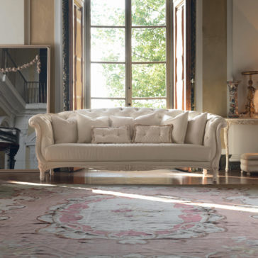 Reproduction Baroque Italian Leather Large 3 Seater Sofa A luxurious living room features a Reproduction Baroque Italian Leather Large 3 Seater Sofa adorned with multiple plush pillows. This elegant piece is centered in front of a tall window, surrounded by ornate decor, a pink patterned rug, and a large mirror reflecting a grand staircase.