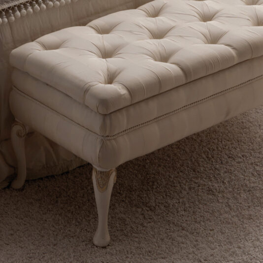Reproduction Designer Italian Button Upholstered Storage Bench The image shows a luxurious Reproduction Designer Italian Button Upholstered Storage Bench, featuring a tufted cream-colored seat and positioned in a room with a carpeted floor. This elegant bench boasts carved wooden legs with ornate detailing and is upholstered in soft fabric.