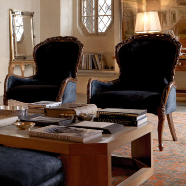 Classic Italian Rose And Ribbon Walnut Armchair Two Classic Italian Rose and Ribbon Walnut Armchairs with dark velvet upholstery are placed in an elegant, traditional living room. A wooden coffee table in front of the chairs holds books and decorative items. A large window, artwork, and a lamp in the background complete the sophisticated setting.