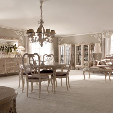Designer Round Italian Dining Table Set A luxurious dining room features the Designer Round Italian Dining Table Set, complete with six matching chairs. A decorative chandelier illuminates the space, while elegant glass cabinets filled with dishware add a touch of sophistication. The room is adorned in neutral tones, featuring intricate wall moldings and a plush carpet covering the floor.