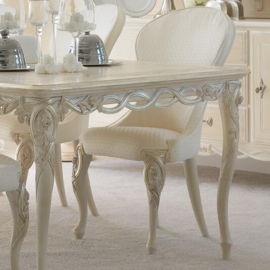Elegant dining area featuring a wooden table with ornate carvings and luxurious Luxurious Designer Italian Dining Chair. The table is set with decorative candle holders and glass-covered candles, complemented by muted neutral colors and classic vintage design elements.