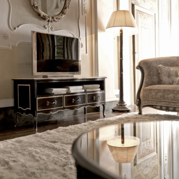 Luxurious Louis Italian TV Unit A luxurious living room with classic-style decor features an ornate lamp, a plush loveseat, and an elegant Luxurious Louis Italian TV Unit with drawers. A large mirror adorns the wall while a soft, fluffy rug and a glass coffee table add coziness to the space.