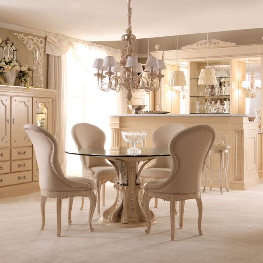 Opulent Italian Dining Chair A luxurious dining room showcases an elegant round glass table with a carved wooden pedestal, surrounded by four Opulent Italian Dining Chairs. A sophisticated chandelier hangs overhead. The room also features a bar area complete with a glassware display and antique-style furniture.