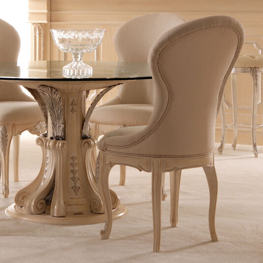 Opulent Italian Dining Chair This elegant dining room features a round glass-top table with an ornate carved base, surrounded by Opulent Italian Dining Chairs. These chairs boast high, curved backs and intricate details. A decorative crystal bowl graces the tabletop, creating a sophisticated and classic ambiance.