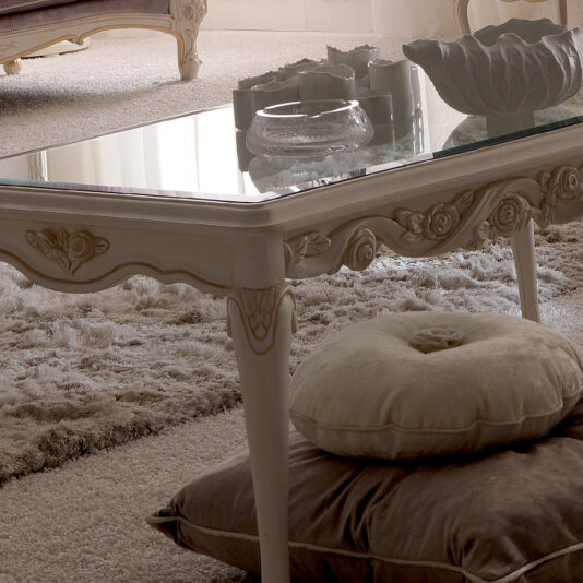 Reproduction Italian Rectangular Coffee Table A chic living room featuring a Reproduction Italian Rectangular Coffee Table with intricate carvings on its legs. On and under the table are elegant cushions. The room is adorned with a plush, textured rug, while soft natural light filters through curtain-draped windows.