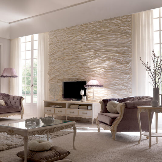 Sophisticated living room featuring a textured wall installation behind a flat-screen TV on a console table. The room is adorned with plush mauve sofas, a glass coffee table with books and cushions, and the elegant Venetian Button Upholstered Italian Armchair. Large windows with sheer curtains and ambient lighting from floor and table lamps enhance the atmosphere.