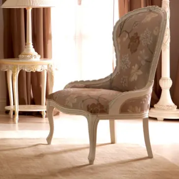 Venetian Style Italian Armchair A Venetian Style Italian Armchair featuring an ornate wooden frame and floral fabric upholstery sits on a beige rug. The chair is positioned in a softly lit room with earth-tone drapes, an elegant side table, and a tall decorative floor lamp in the background.