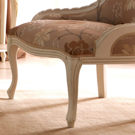 This Venetian Style Italian Armchair boasts elegant vintage design with intricate carvings and cream-colored wooden legs. The seat and backrest are adorned with a floral-patterned fabric in shades of brown and beige, imparting a classic charm to the furniture piece. It is beautifully displayed on a light-colored carpet.