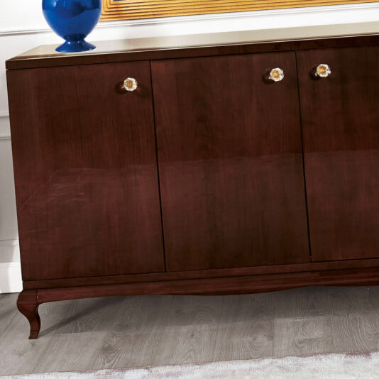 High end Modern Glamour large Wenge Sideboard A High end Modern Glamour large Wenge Sideboard with three doors and crystal knobs stands elegantly on a grey laminate floor, adorned with a blue vase on top. The sideboard is partially reflected in a large framed mirror above it, exuding modern glamour.