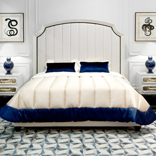 A luxurious bedroom boasts a spacious High End Modern White Ottoman Storage Bed adorned with blue and white bedding. It is flanked by two nightstands featuring blue table lamps, while a geometric-patterned rug enhances the floor and framed art pieces adorn the walls.