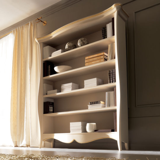 An elegant, vintage-style Large Italian Luxury Freestanding Bookcase stands against a wall. The bookcase has open shelves filled with neatly stacked books and decorative items. Light from a nearby large window with sheer curtains highlights the soft, warm tones of the room.
