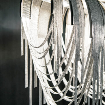 Contemporary Glamorous Rectangular Chain Chandelier The Contemporary Glamorous Rectangular Chain Chandelier features overlapping silver chains cascading in loops, creating a shimmering effect against a dark background. The elegant design resembles draped jewelry in a chandelier form.