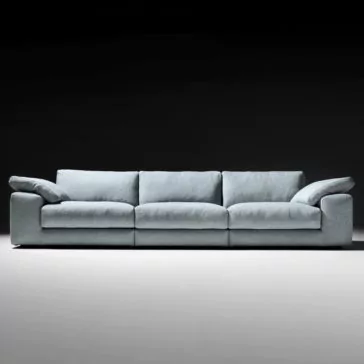 Large Linen Designer Modular Sofa The Large Linen Designer Modular Sofa, boasting a modern light blue hue with three seat cushions and padded armrests, is showcased against a dark, gradient background. This designer sofa features a low-profile design and exudes both comfort and spaciousness.