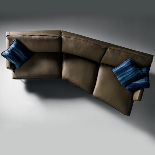 Modern Leather Modular Sofa Top view of the Modern Leather Modular Sofa, featuring an L-shaped design with three seat cushions and two blue decorative pillows. The brown leather sectional sits against a plain gray background, casting a shadow on the floor.