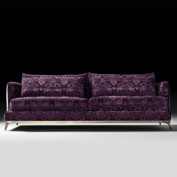 The Velvet Luxury Modern Sofa, upholstered in deep purple velvet with intricate damask patterns and equipped with two large back cushions, showcases sleek modern design and silver metal legs against a black background.