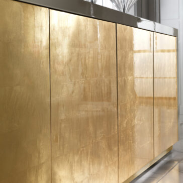 Large High End Gold Leaf Sideboard Close-up of the Large High End Gold Leaf Sideboard featuring shiny metallic gold doors and a glossy dark countertop, reflecting light in a contemporary interior.