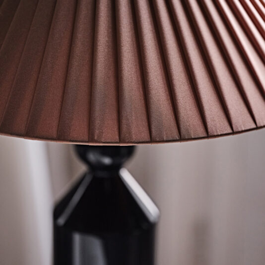 A close-up of the Classic Designer Luxury Table Lamp showcases its pleated reddish-brown lampshade and glossy black geometric base. The softly blurred background enhances the warm and intimate ambiance.
