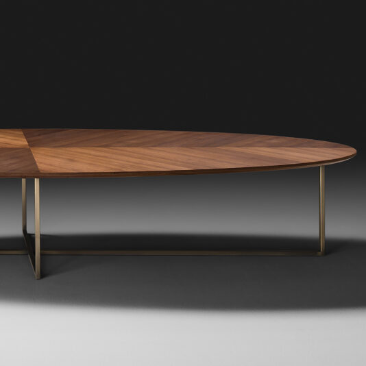 The Contemporary Walnut Oval Coffee Table features a sleek design with a geometric patterned surface and minimalist metal legs. Set against a dark background, the table's finish beautifully highlights the natural wood grain, while the metal legs provide a simple and unobtrusive frame.