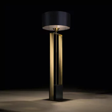 The Gold Contemporary Designer Floor Lamp features a sophisticated, modern design with a tall, rectangular gold base and an oversized, cylindrical black lampshade that emits a soft, warm light. This exquisite piece stands against a dark background, casting a subtle glow on the floor.