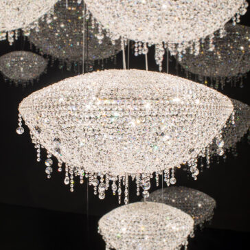 Top Dressed Contemporary Crystal Chandelier A Top Dressed Contemporary Crystal Chandelier adorned with shimmering droplets hangs against a dark background. This elegant oval-shaped piece, accompanied by smaller chandeliers, creates a luxurious atmosphere.