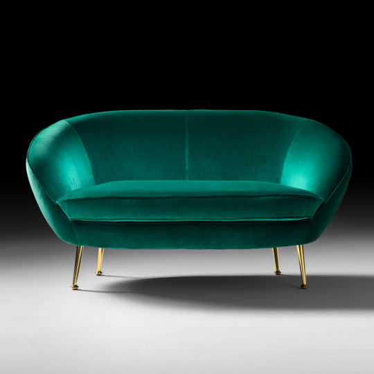 A plush, teal velvet Contemporary Designer 2 Seater Sofa featuring a rounded back and slender gold legs. The backdrop transitions from dark to light, accentuating the loveseat's elegance and rich color. The overall design exudes modern luxury.
