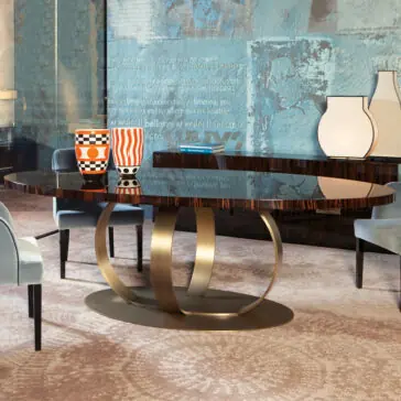 Contemporary Italian Bronzed Ring Oval Dining Table A modern dining room features a sleek metallic base Contemporary Italian bronzed ring oval dining table adorned with two geometric-patterned orange and black vases, surrounded by light blue upholstered chairs and accented with abstract wall art.