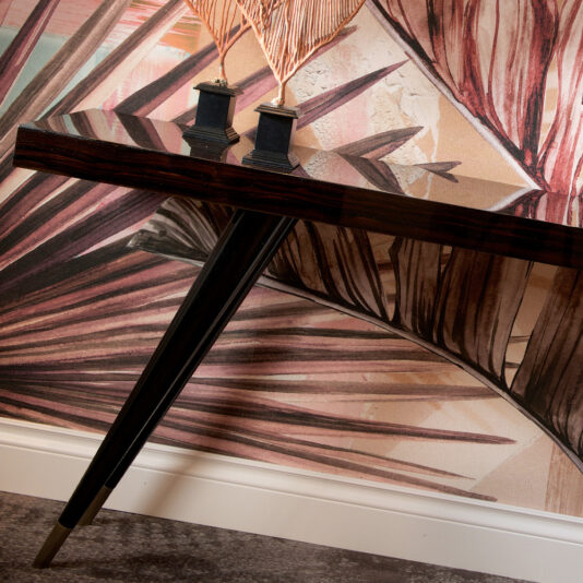 Contemporary Italian Rectangular Console Table A Contemporary Italian Rectangular Console Table with black angled legs is set against a wall with pink and tan tropical leaf-patterned wallpaper, topped with two feather-like decorative ornaments.