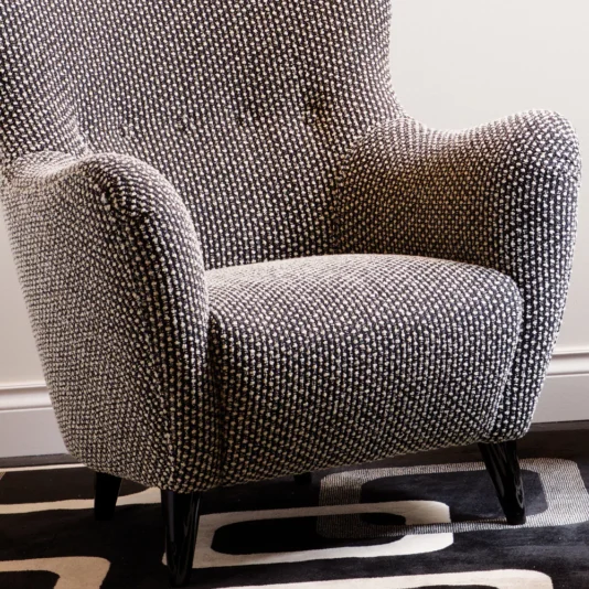 Luxury High End Designer Armchair A Luxury High End Designer Armchair with a plush high backrest and rounded arms sits on a black and white geometric rug, featuring textured fabric and dark, slightly tapered legs.