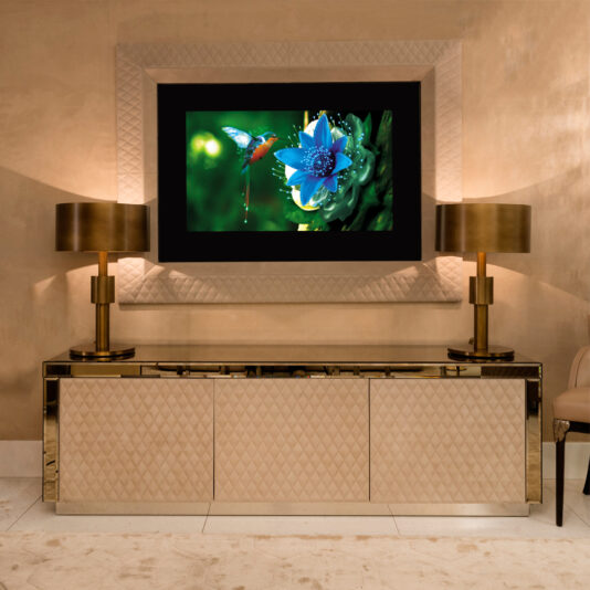 The Luxury High End Wall Mounted TV and Media Unit Set showcases a blue flower and hummingbird, elegantly framed by a decorative border. A quilted-front media unit stands below, flanked by two gold lamps, completing the sophisticated modern design with warm brown tones.