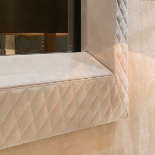Luxury High End Wall Mounted TV and Media Unit Set Close-up of a quilted, diamond-patterned beige fabric panel at an angle. This luxury piece is part of the Luxury High End Wall Mounted TV and Media Unit Set, with soft shadows that enhance its texture and design, perfect for complementing your decor.