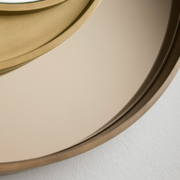 Modern Italian Designer Offset Circles Mirror Close-up of the Modern Italian Designer Offset Circles Mirror, which showcases an offset circular design with a gold-toned frame at the top edge and a muted gray frame towards the bottom. This designer mirror reflects a minimalistic interior and is mounted on a white-textured wall, exemplifying sleek contemporary elegance.