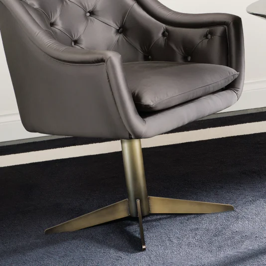 The Italian Button Upholstered Satin Dining Chair, featuring a modern gray swivel design with a cushioned seat and button-tufted backrest on a metal base, sits elegantly on a dark carpet near a white wall.