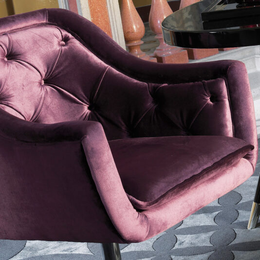 An Italian Button Upholstered Velvet Dining Chair in rich purple, featuring a tufted backrest and chrome legs, elegantly complements a glossy black table on a patterned carpet.