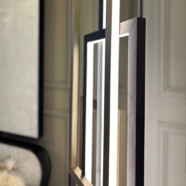 Italian Geometric Designer Modern Floor Lamp Close-up of the Italian Geometric Designer Modern Floor Lamp composed of rectangular frames with LED lighting. The lamp casts shadows on a paneled wall in a minimalist interior, revealing sleek dark and light-colored finishes on the furniture and other decor elements.