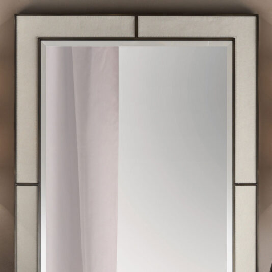 An Italian Designer Leather Wall Mirror with a unique, geometric beige frame is mounted on a wall. The leather frame is divided into two sections: one bordering the top and left edges and the other bordering the bottom and right edges. A faint reflection of a curtain is visible in the mirror's surface.
