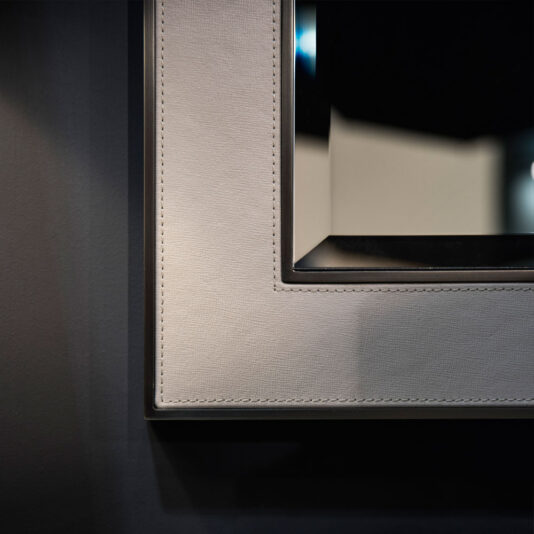 Close-up of a photo frame with a dark background. The frame, echoing the design of an Italian Designer Leather Wall Mirror, boasts a textured finish with visible stitching around the edges. Inside, the photo displays a minimalistic, blurred image. A light source casts a subtle glow on the frame.