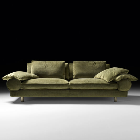 The Contemporary Retro Inspired Designer Sofa, upholstered in green velvet with round armrests and silver legs, is centered against a black background. It is furnished with two large seat cushions, two backrest pillows, and two matching throw pillows resting on the arms, exuding a retro-inspired elegance.